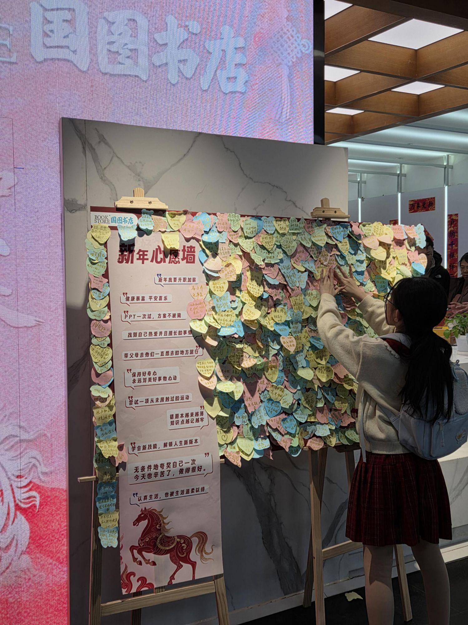 小朋友把自己写下的新年愿望便利贴贴到展板上。
